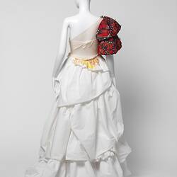 Back view of white ruffled wedding dress with oversized red butterfly-like right shoulder detail.