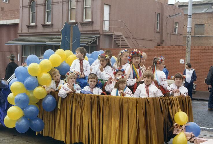Group of children on a street procession float, waving and wearing Ukrainian national dress.