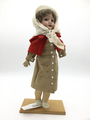 A doll dressed as a nurse in a brown dress, red capelet and white scarf