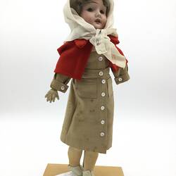A doll dressed as a nurse in a brown dress, red capelet and white scarf