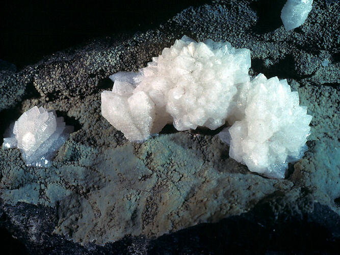 Pale cream crystals on a grey rock.