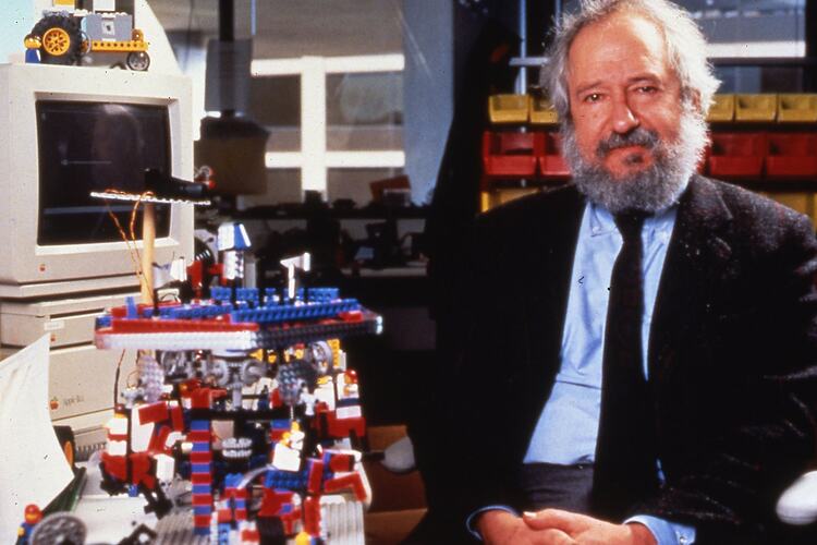 Seated man wearing dark jacket and tie. Lego construction and computer beside him.