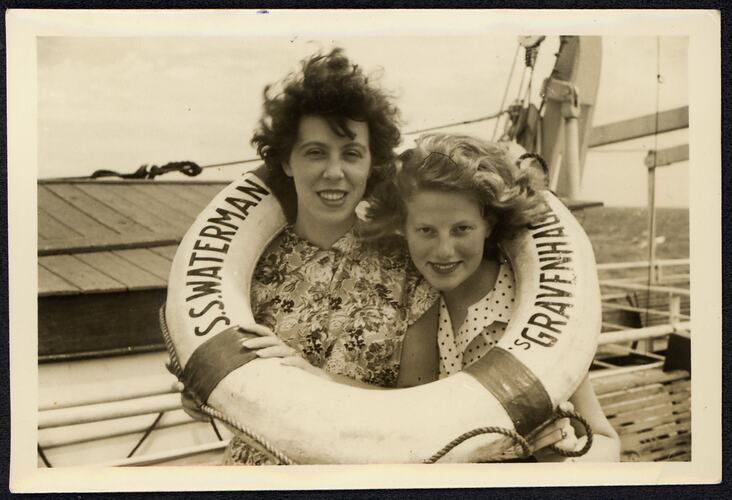 Two women smile and posing in a life ring onboard a ship.