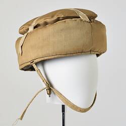 Beige cotton cap, padded, with strap. Three quarter front view.