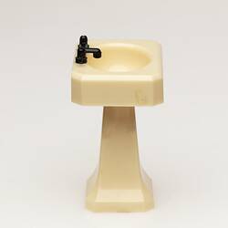 Toy bathroom sink made of cream coloured moulded plastic. Two faucets. Profile.