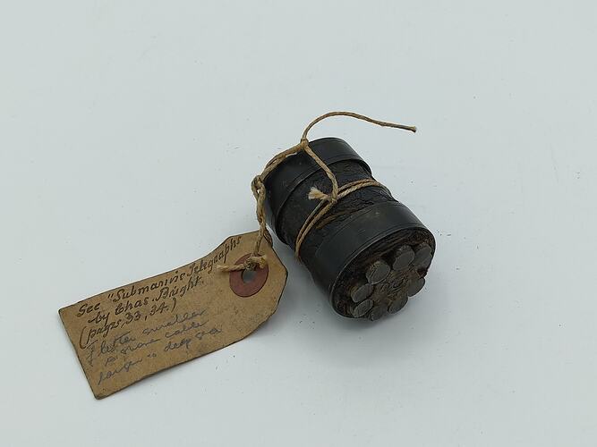 Section of metal cylinder containing metal cables. Paper tag attached.