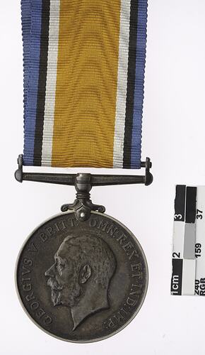 Round medal with profile of man and text surrounding, with multicoloured ribbon.