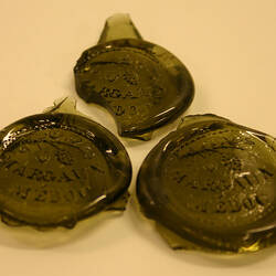 Three glass bottle seals with lettering.
