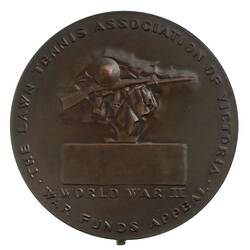 Round bronze medal with rifle, helmet and garment above plaque. Text below and around,