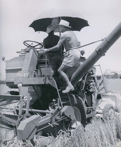 Men standing on harvester in a field.