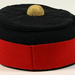 Black wool hat with red wool band around rim and yellow decoration in top centre.