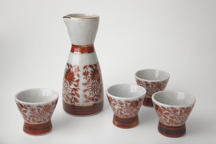 Sake jug and cup set with intricate gold and deep orange floral design.
