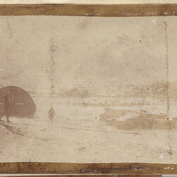 Snowy landscape with cylindrical hut and two men walking in midground.