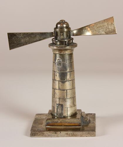 Silver lighthouse paperweight with engraved light beams extending from the windows on each side.