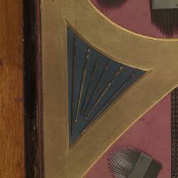 Detail of panel made of needles, crochet hooks, surgical needles, and other needles and needle cases. In red, black and yellow.