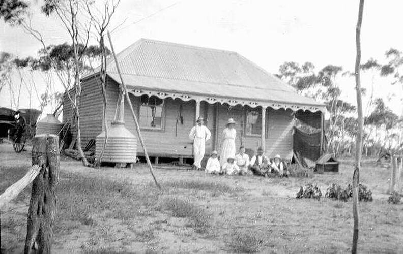 An old homestead with a family in white clothes in front of it.