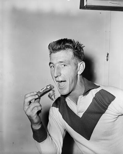 Footballer posing and about to take a bite of a chocolate bar.