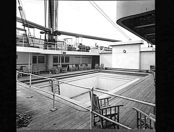 Ship deck with empty rectangular swimming pool. Chairs around edge.