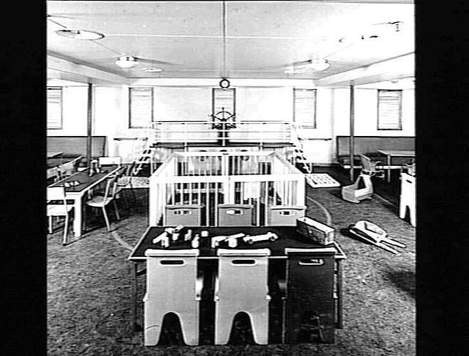 Ship interior. Children's playroom. Small table and chairs at front. Playpen behind.