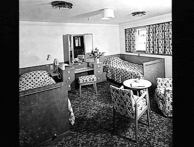 Ship interior. Two single beds against each wall. Dressing table, two chairs and coffee table.
