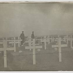 Two soldiers standing in graveyard marked with white crosses.