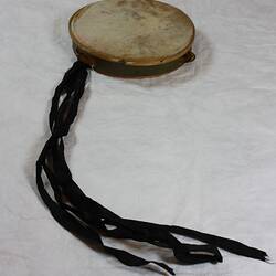 Tambourine, olive frame, natural animal skin. Metal jingles, bells and black ribbon streamers.