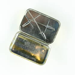 Yellow metal rectangular box, lid off. Contains 3 metal cannulae.