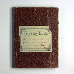 Closed book with brown cover and dark blue spine, cover reads 'Exercise Book', with written red text below.
