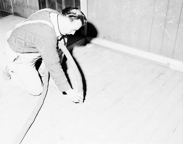 Monochrome photograph of a man laying flooring.