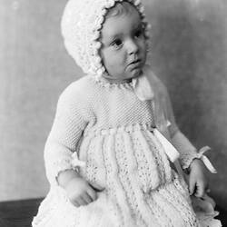 Female toddler in knitted dress and bonnet.