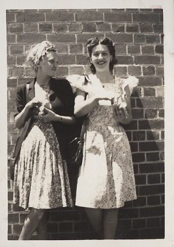 Two girls posing against brick wall.