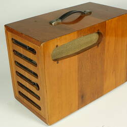 Control panel housed in wooden box with slats at one end and handle on top.