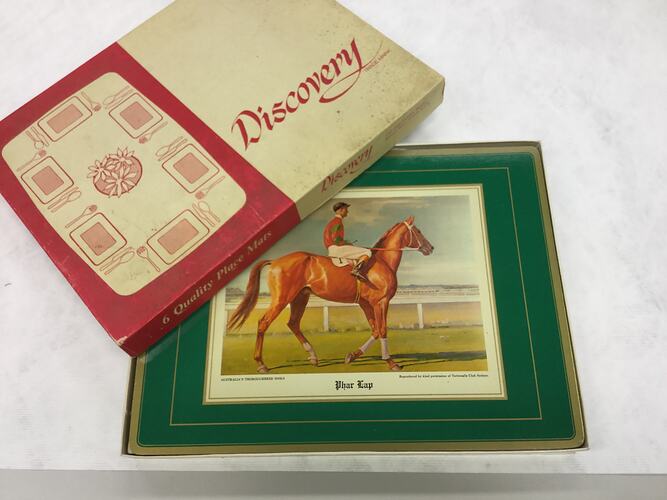 Open box with placemat featuring racehorse. Green frame. Lid has red and white table setting.