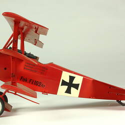 Red aeroplane model. White strip on top of wings with black cross. Left profile.