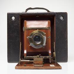 Brown leather-covered camera. Fold out wooden centre, red leather bellows behind lens.