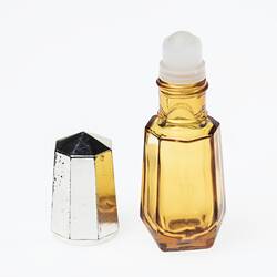 Yellow angular glass bottle with metal lid off. Bottle has plastic roller applicator.
