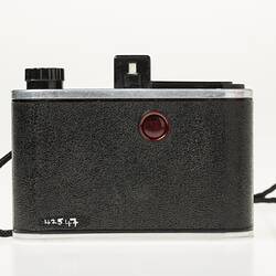 Black camera with metal trim. Back view with red button. Black wrist strap.