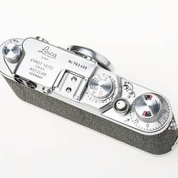 Black camera with metal trim, lens, dials at top corners. Top view.