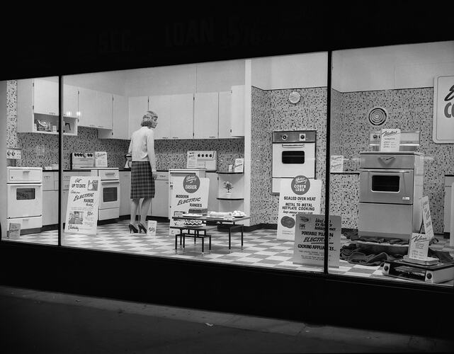 View through shop window of woman looking at display kitchen and appliances.