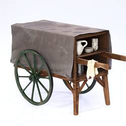 Miniature wooden coffee hand cart with two wheels, two legs. Internal shelf has coffee items, jug, cups, tin.