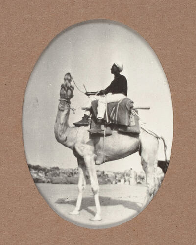 Man seated on camel with saddle.