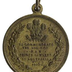 Medal with text framed by wreath of eucalypt and oak. Above is Prince of Wales' plume. Loop and ring at top.