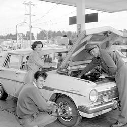 Woman and two men servicing a car at a petrol station.