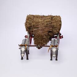 Front view model of two grey bullocks pulling a hay wagon with haystack and red wheels.