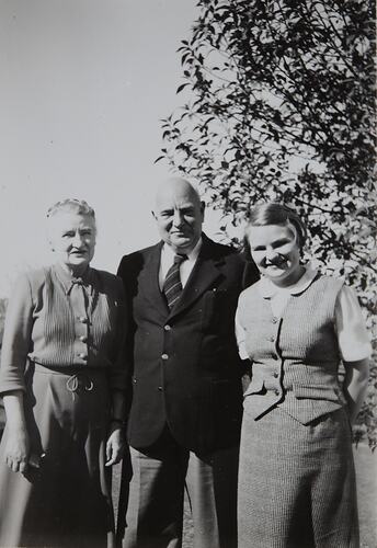 Older man and woman stand with young woman outdoors. Three quarter length.