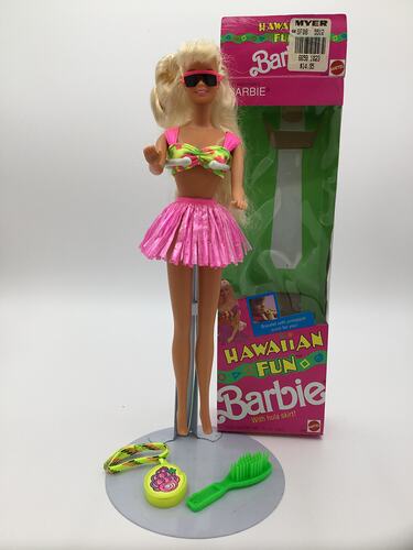 Blonde Barbie doll with box. Wears pink bikini top and skirt and sunglasses. Accessories at her feet.