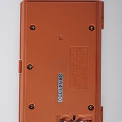 Back of orange plastic, handheld game console, rectangular, closed. Hinge at right.