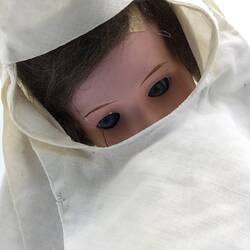 The face of a doll dressed as a nun in a grey dress and white veil
