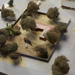 Model detail, aerial view of red-roofed building surrounded by trees. Carpark around it.