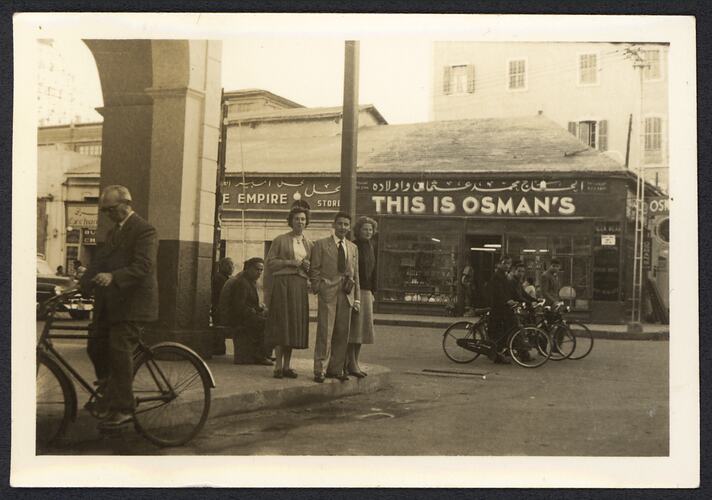 Man and two women standing on street corner as bikes ride past.